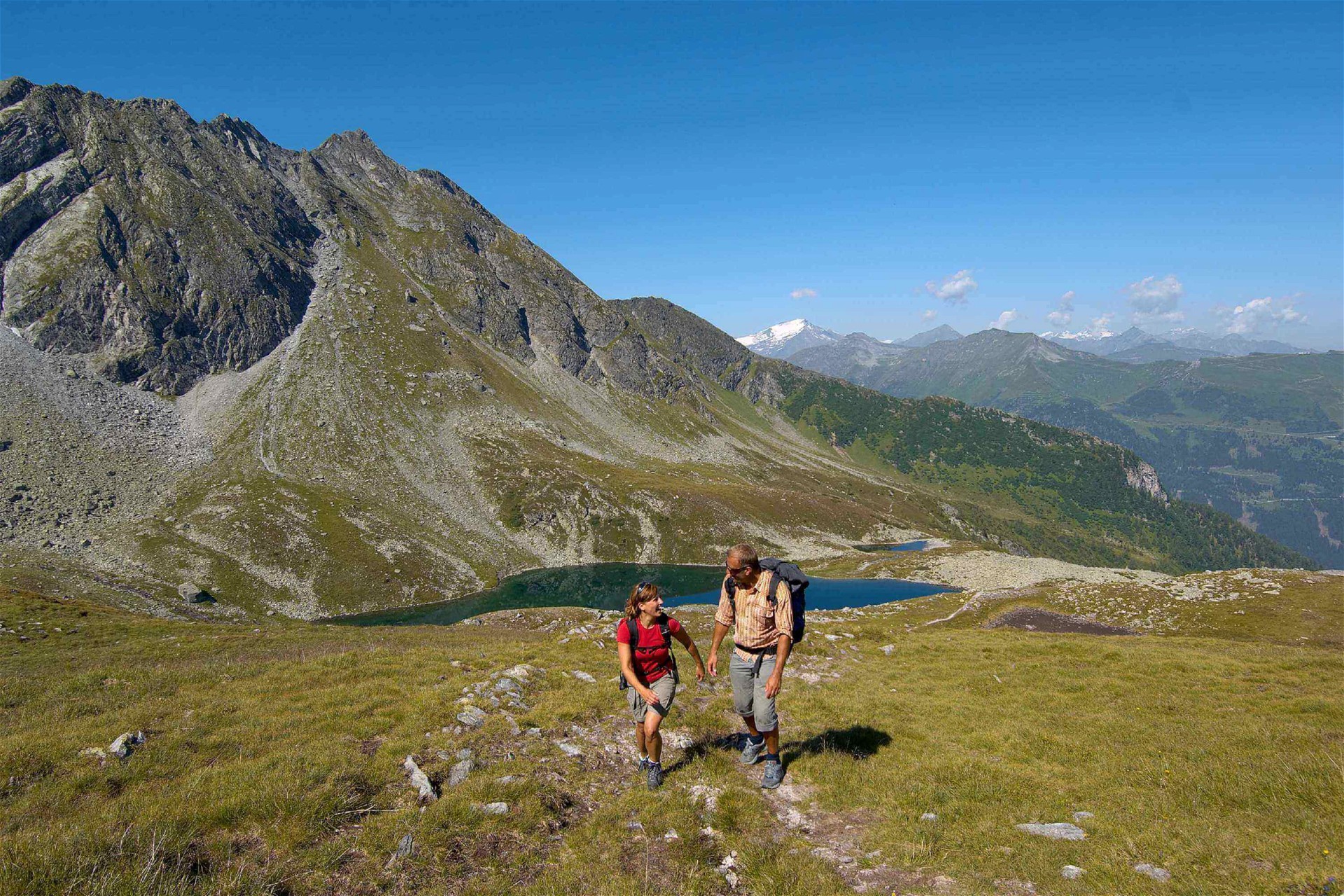 Frau und Mann wandern während ihres Sommerurlaubs im Salzburger Land an einem kleinen Bergsee vorbei