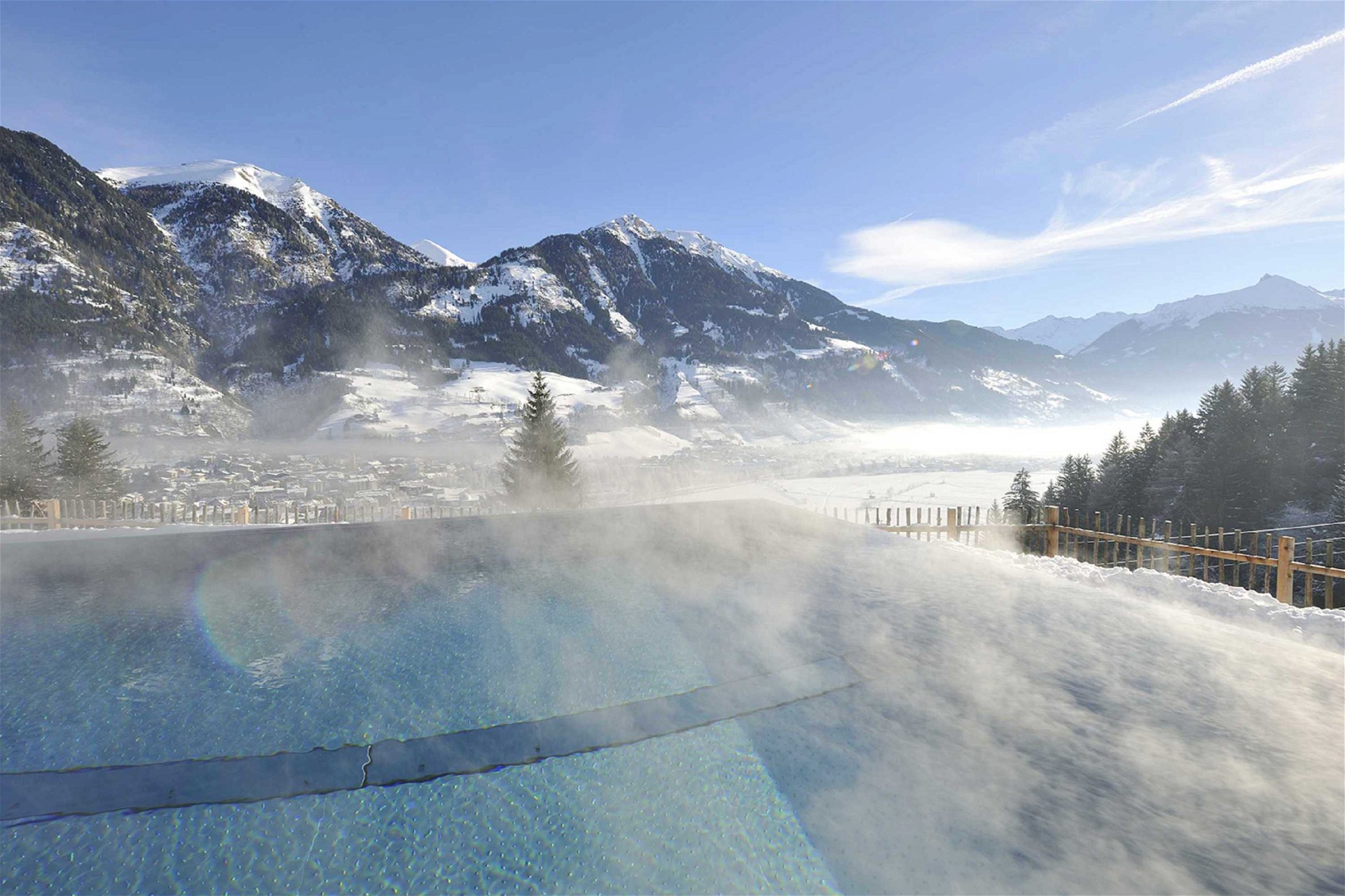 Dampfender Infinity Pool im Winter mit verschneiter Berglandschaft im Hintergrund