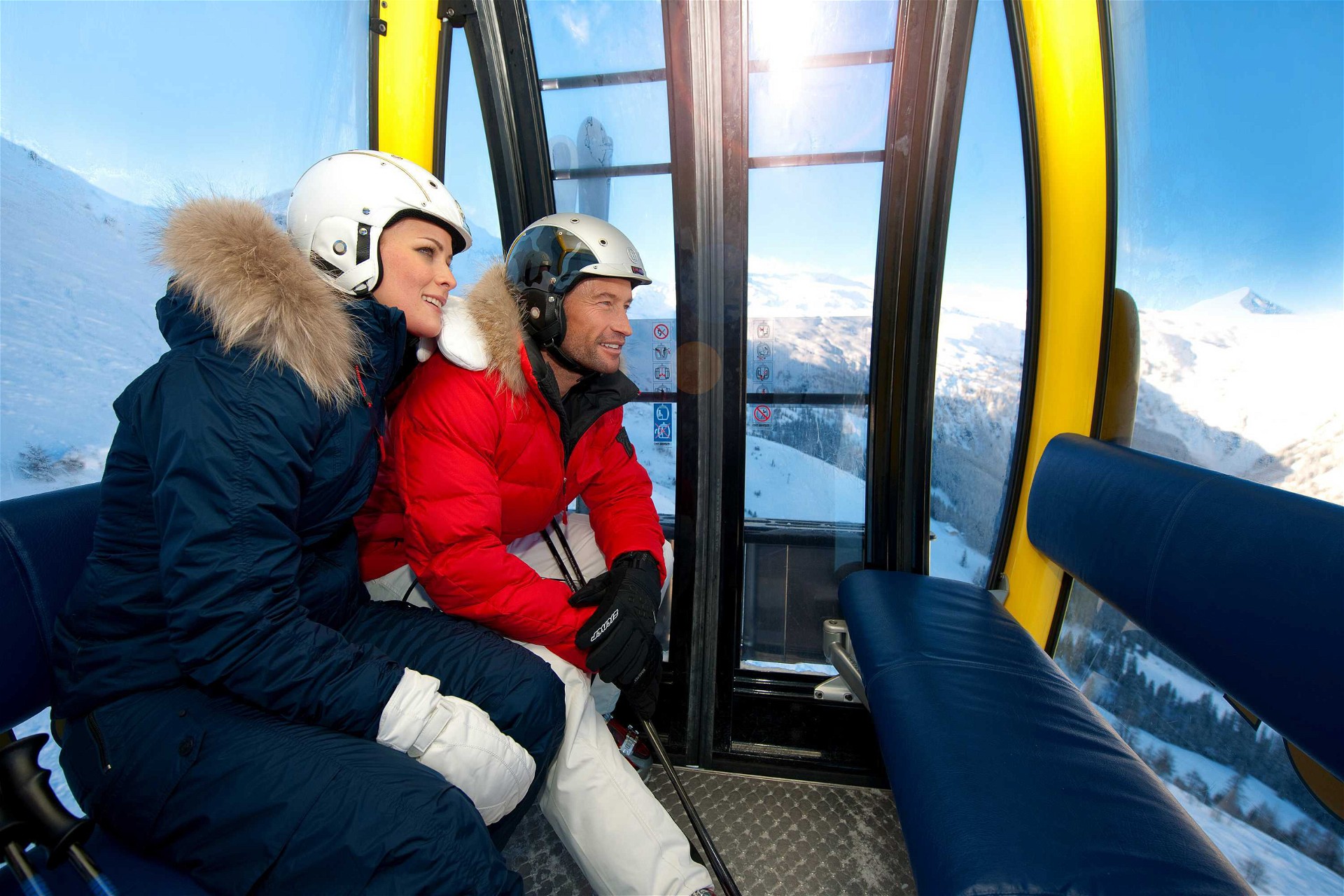 A couple in ski gear sits in a gondola and enjoys the view
